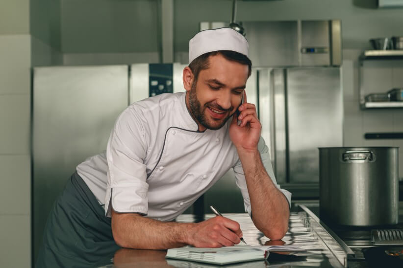 A chef speaking on the phone writing down a supply order