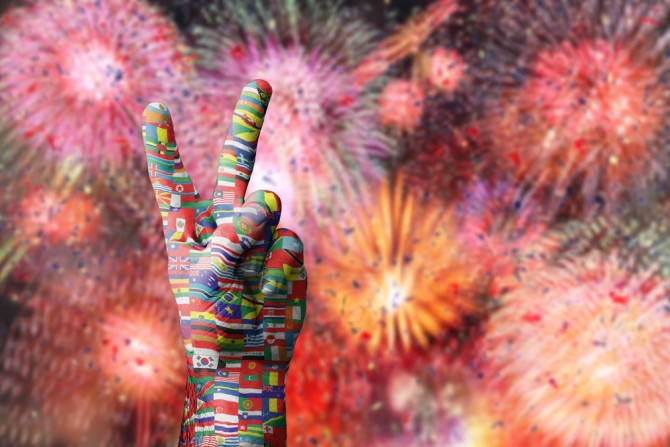 hand in peace sign covered in international flags with fireworks display in background