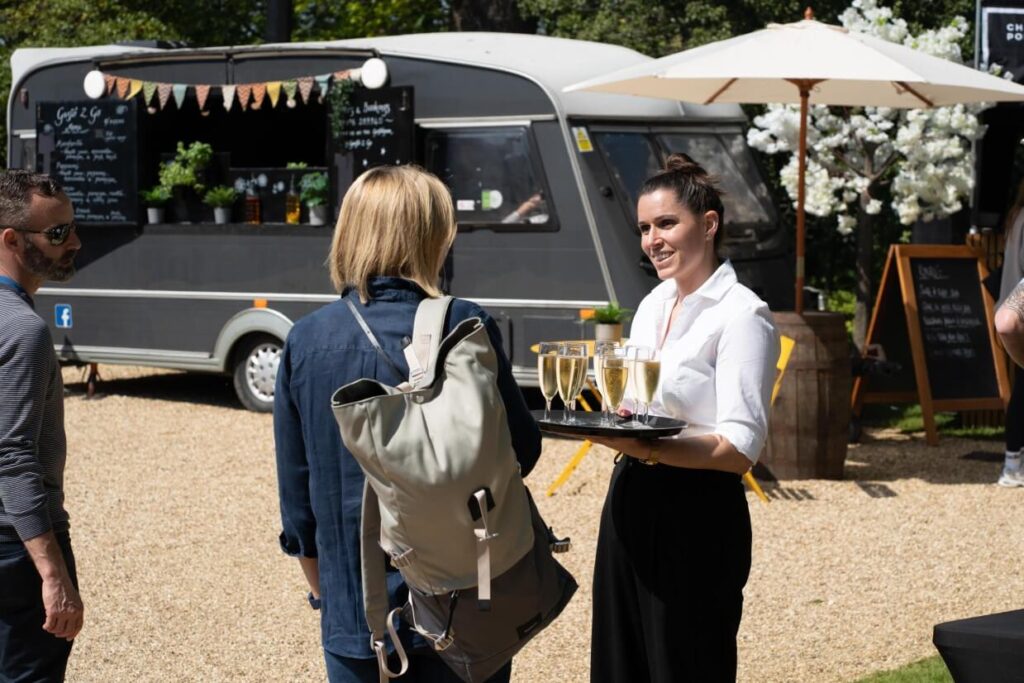 a girl catering guests outside with a tray of drinks.